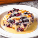 Freshly baked blueberry lemon butter swim biscuit drizzled with tangy lemon glaze, served warm on a white plate.