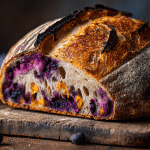 Blueberry Orange Sourdough Bread loaf with a golden crust and a slice cut open to show a purple-speckled crumb and orange zest.