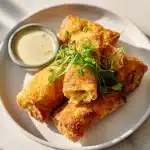 Golden-brown Irish egg rolls with corned beef, cabbage, and cheese, on a white plate with horseradish sauce.
