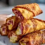 Golden brown crispy Reuben egg rolls on a plate, with a side of creamy thousand island dipping sauce, caraway seeds visible on the wrapper.