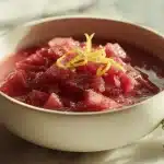 A white bowl of deep pink stewed rhubarb compote on a marble surface