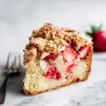 A slice of strawberry rhubarb coffee cake with buttery streusel and fruit filling, on white marble with a silver fork.