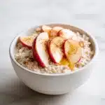 Warm bowl of apple cinnamon prebiotic oatmeal with fresh apple slices, honey drizzle, and cinnamon on a white marble surface.