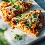 A close-up of a BBQ Chicken Flatbread Recipe on a round wooden board, showcasing melted mozzarella, barbecue chicken, and red onion.