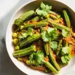 Appetizing bowl of slime-free bhindi okra curry recipe with vibrant green okra, rich tomato masala, and fresh cilantro on a bright surface.