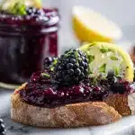 Two mason jars of homemade blackberry jam with fresh blackberries on marble