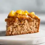 A slice of brown sugar peach cake with caramel frosting and fresh peaches on marble, showing brown sugar peach cake recipe.