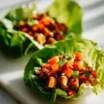 Cashew Chicken Lettuce Wraps in butter lettuce cups with glossy hoisin chicken, golden cashews, and diced carrots on marble.
