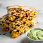 Golden crispy Corn and Black Bean Quesadillas with Avocado Crema, filled with corn and black beans, served with green avocado crema.