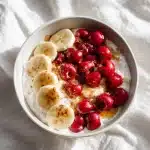 Creamy cottage cheese sleep bowl topped with tart cherries, banana slices, honey, and cinnamon, photographed in natural light.