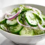 Cucumber salad recipe showing translucent green cucumber slices, purple onion rings, and fresh dill tossed in a light vinegar dressing.