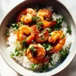 A top-down overhead shot of garlic brown sugar shrimp with a glossy caramelized glaze, scattered parsley, and steaming jasmine rice in a white bowl, brightly lit.