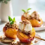 Grilled peach halves with caramelized brown sugar, crunchy pecans, vanilla ice cream, and fresh mint on a bright surface.