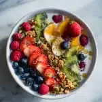 A gut health smoothie bowl with raspberries, kiwi, granola, seeds, and honey drizzle in a ceramic bowl.