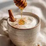 Steaming honey cinnamon bedtime drink in an artisan mug with golden honey drizzle, a cinnamon stick inside, and spice dusting on a cozy table.