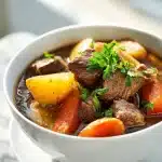 A steaming bowl of Irish stew with tender beef, chunky vegetables, and a glossy Guinness broth, topped with fresh parsley.
