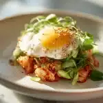 Kimchi eggs with sunny-side-up egg over white rice bowl topped with scallions