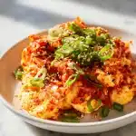 Fluffy kimchi eggs scrambled with vibrant fermented kimchi, garnished with sliced scallions and toasted sesame seeds, served on a white plate.