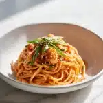 A plate of creamy kimchi spaghetti, a kimchi pasta dish, garnished with scallions and sesame seeds in natural window light, ready to eat.