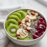 A white bowl filled with a kiwi sleep bowl: yogurt, sliced kiwi, banana, almonds, chia seeds, and tart cherry juice, on marble.