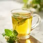 Steaming ceramic mug filled with golden lemon balm tea for sleep, garnished with fresh green lemon balm leaves and white chamomile flowers on a bright wooden table.