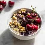 A warm bowl of melatonin rich cherry oatmeal with tart cherries, walnuts, and chia seeds, on a rustic wood table with soft morning light.