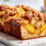 Sliced peach bread with cinnamon crumb topping on a wooden board