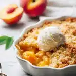 Warm peach cobbler with cake mix in a baking dish, golden buttery topping, a scoop of melting vanilla ice cream, cozy kitchen background.