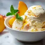 Homemade peach ice cream scooped into a white ceramic bowl with honey drizzle