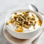 Creamy Greek yogurt bowl sprinkled with pumpkin seeds, drizzled honey, and cinnamon, a pumpkin seed sleep snack on marble surface.