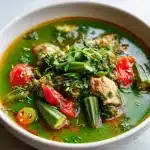 A steaming bowl of vibrant green okra soup with tender chicken pieces, red tomato broth, and fresh herbs, shot in natural light.