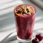 Creamy pink sleep friendly evening smoothie with almond butter drizzle, pumpkin seeds, cinnamon, and tart cherries on marble.