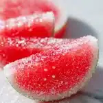 Close-up of bright pink sour watermelon gummies coated in sour sugar on a wooden board, showcasing a homemade sour watermelon gummies recipe.