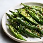 Crispy stir fry okra recipe dish with garlic, ginger, sesame seeds, and scallions on a stoneware plate, no slime.