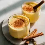 Mug of golden warm almond milk for sleep with cinnamon and honey drizzle, by a candle on a soft knitted blanket, calming bedtime scene.