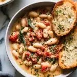White Bean & Tomato Skillet: creamy white beans and chunky tomatoes in garlic-herb sauce, served with crusty bread on a wooden table.