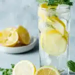 A crystal-clear glass filled with a baking soda recipe for weight loss tonic, featuring floating fresh lemon slices and green mint leaves, set on a bright, airy kitchen counter with natural light.